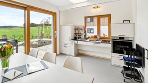 Una cocina moderna con armarios blancos, horno empotrado y vistas a un campo verde.