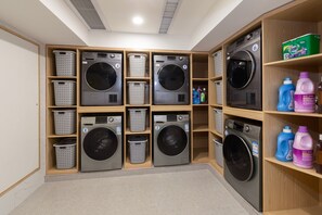 A laundry facility with multiple washing machines and baskets, and shelves with detergent bottles. - Grand Yuntian Yue Hotel Shenzhen Shekou  (Shenzhen)