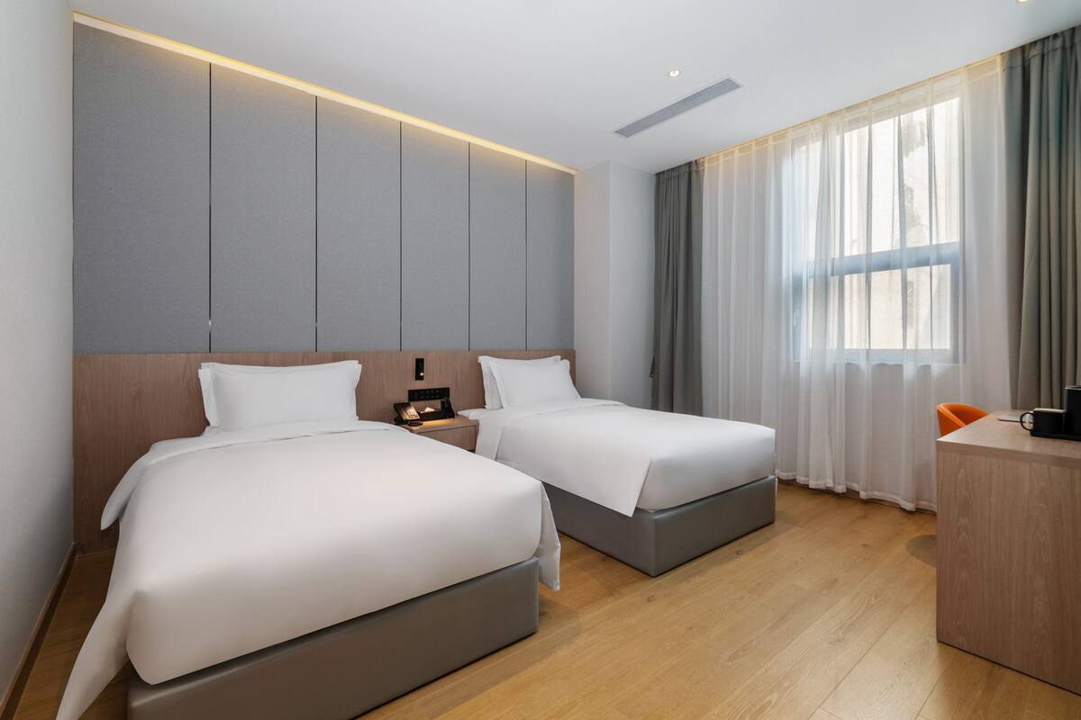 A hotel room with two beds, a desk, and a large window with curtains.