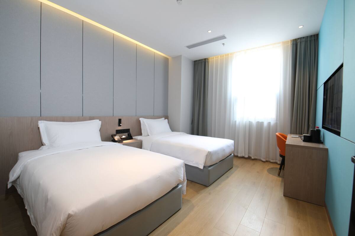 A hotel room with two beds, a desk, and a TV.