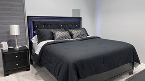 A modern bedroom with a black bed, a nightstand with a lamp, and a large mirror.