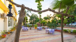 An outdoor seating area with tables and chairs, surrounded by potted plants and trees. - Gharial Bagh Resort (Sawai Madhopur)