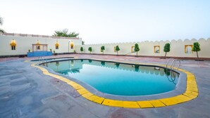 A swimming pool with a yellow safety border, surrounded by a low wall with small windows and decorative elements. - Gharial Bagh Resort (Sawai Madhopur)