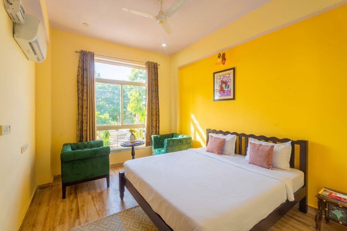 A hotel room with a bed, two green armchairs, a small table, and a window with curtains.