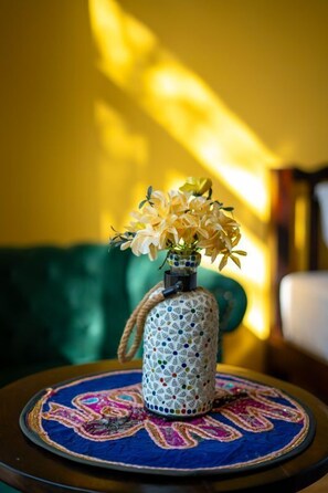Un jarrón decorativo con flores sobre una mesa redonda con mantel estampado en azul y rosa.