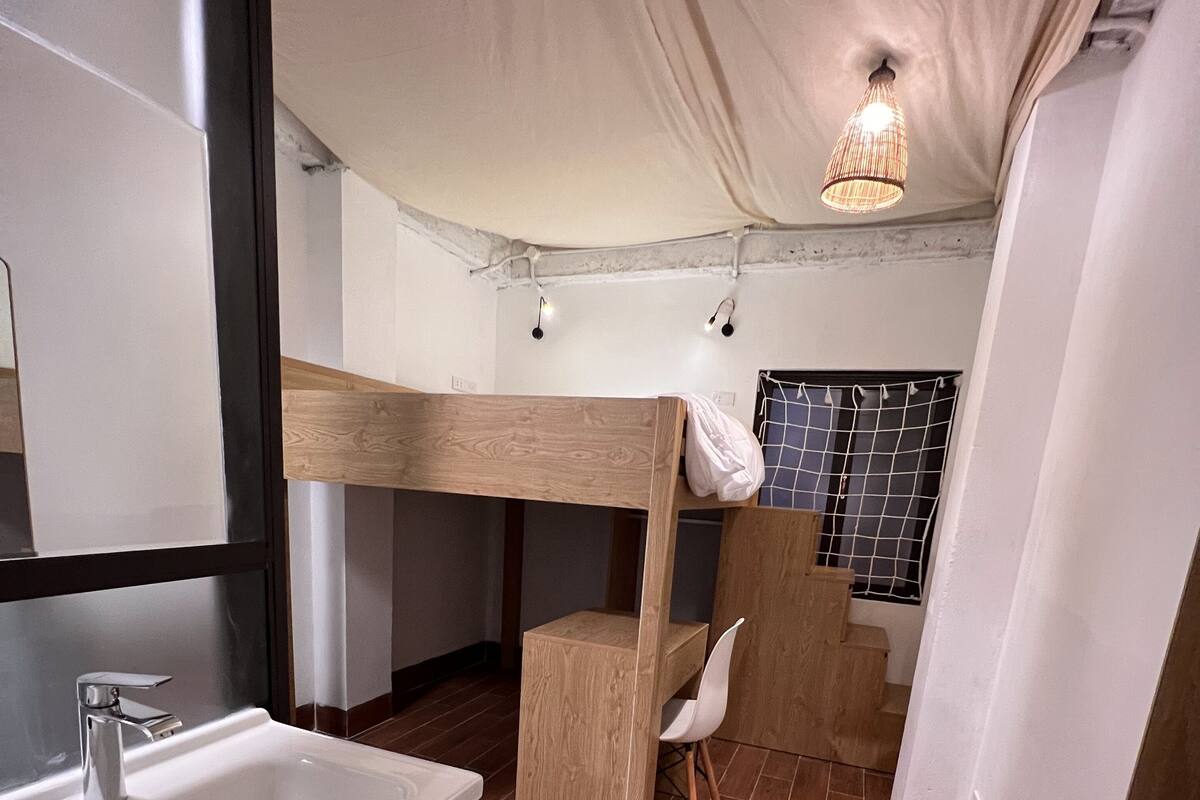 A compact bathroom with a wooden bunk bed, a sink, and a mirror.