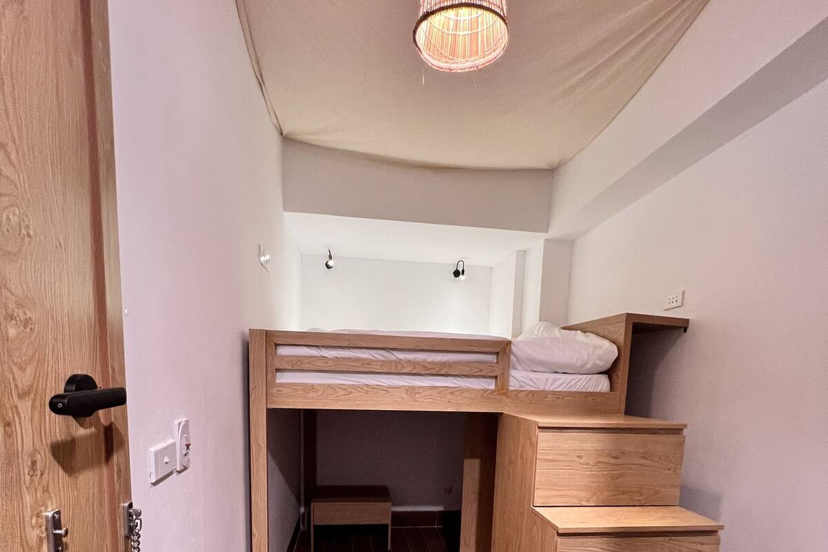 A compact room with a bunk bed, wooden staircase, and a hanging light fixture.