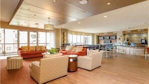 A spacious living area with a kitchen in the background, large windows, and a high ceiling.