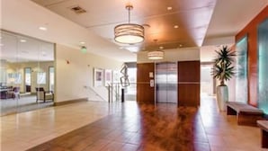 A spacious lobby with a wooden floor, a reception desk, and a staircase leading to an elevator.