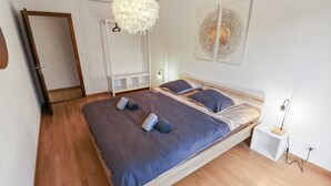 Et soveværelse med en seng, et hvidt skab, en hængende lampe og et billedværk på væggen.