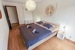 A bedroom with a bed, a white wardrobe, a hanging light fixture, and a wall-mounted artwork.