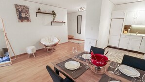 Et spiseområde med et træbord dækket til fire personer, en rød skål og en hvid polstret stol.