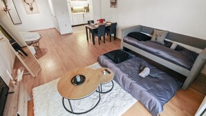 En moderne stue med en grå sofa, et spisebord med stole, et lille træbord med to stole, og en hvid måtte.