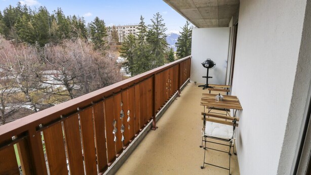 En balkon med gelænder i træ, et lille bord med en lampe og et tøjstativ.
