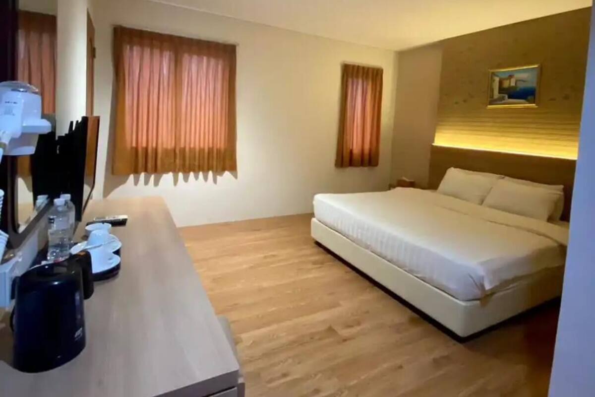 Hotellihuone, jossa on sänky, peilillä varustettu työpöytä ja kaksi ikkunaa, joissa on verhot.