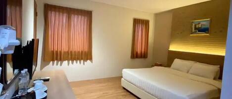 A hotel room with a bed, a desk with a mirror, and two windows with curtains.