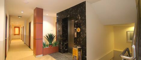 Um saguão de hotel com uma recepção de mármore, uma planta e uma placa de saída.