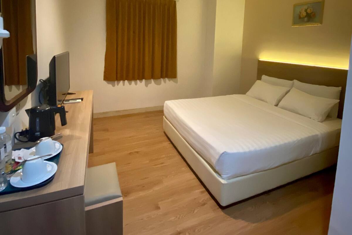 Hotellihuone, jossa on sänky, työpöytä tietokoneella, kahvinkeitin ja taulu seinällä.
