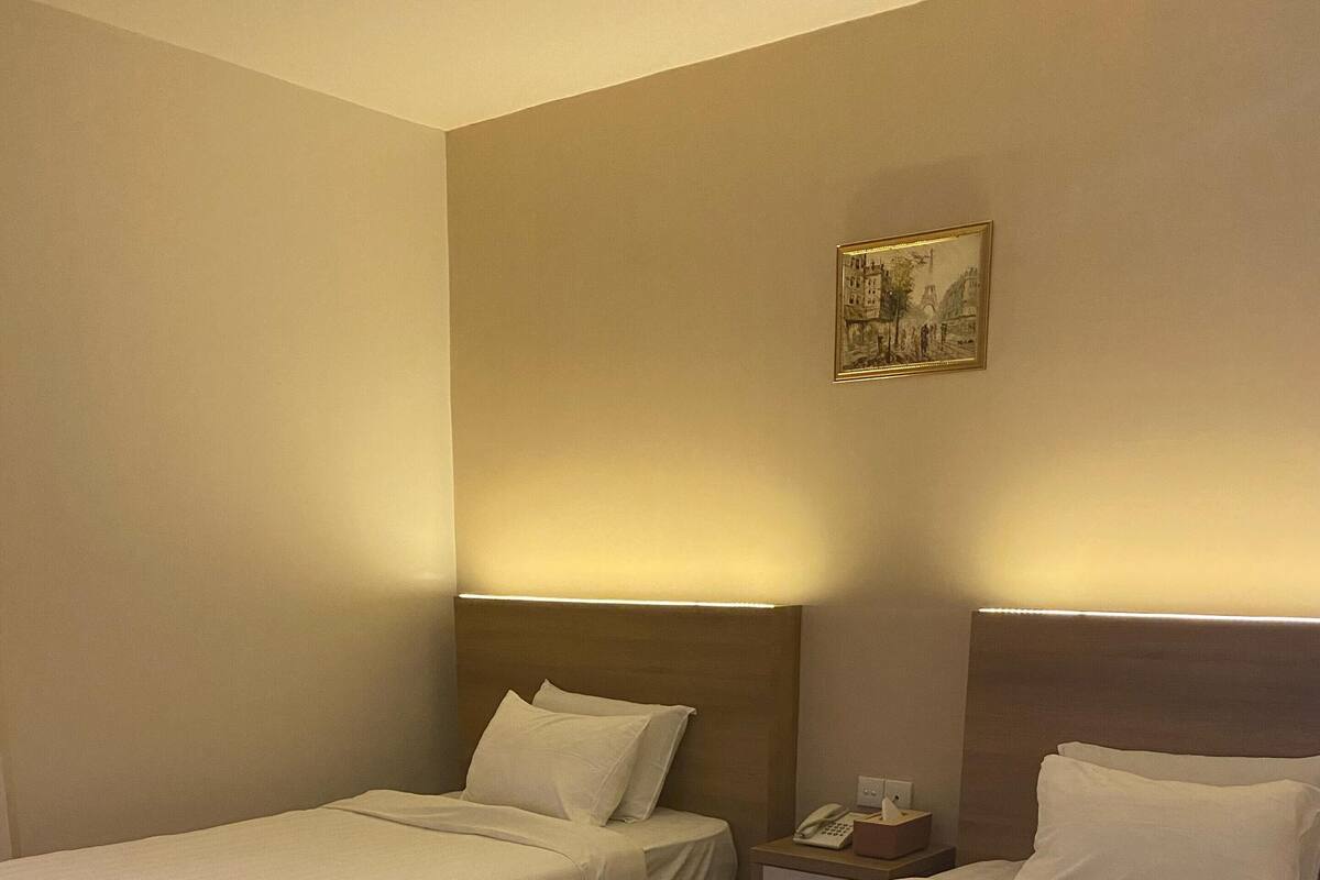 Hotellihuone, jossa on kaksi sänkyä, puulattia sekä yöpöytä, jossa on puhelin ja paperinenäliinoja.