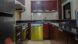 A kitchen with a stainless steel refrigerator, a dishwasher, and wooden cabinets. - Adorable 1BDR apartment in Sport City (Dubai)