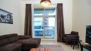 A living room with a sofa, a chair, a small table, a TV, and a large window with curtains. - Adorable 1BDR apartment in Sport City (Dubai)