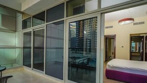 A modern hotel room with large sliding glass doors, a bed, a small table, and a chair. - Adorable 1BDR apartment in Sport City (Dubai)