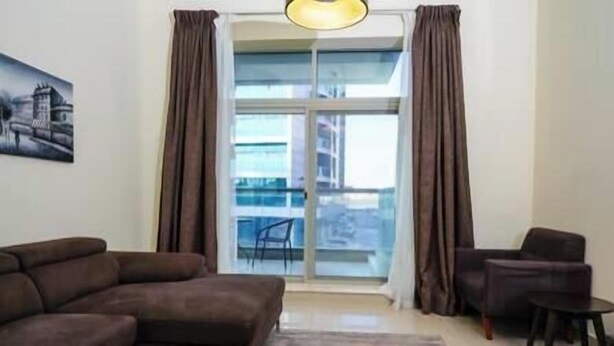 A living room with a sofa, a chair, a small table, and a large window with curtains. - Adorable 1BDR apartment in Sport City (Dubai)
