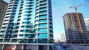 A modern high-rise building with a curved facade, multiple balconies, and a construction crane in the background. - Adorable 1BDR apartment in Sport City (Dubai)