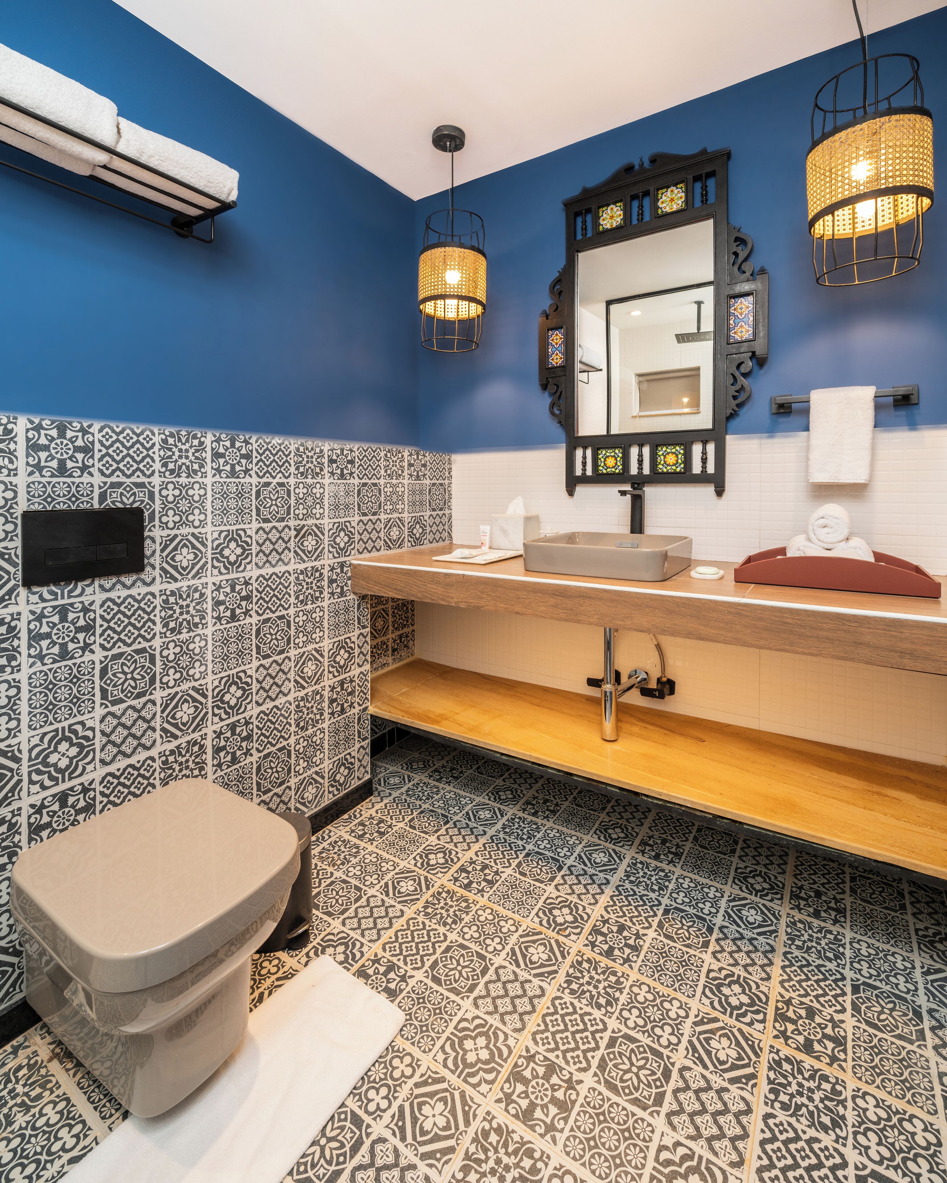 A bathroom with a blue wall, patterned tiles, a wooden vanity, a white sink, a mirror, and two hanging lights.