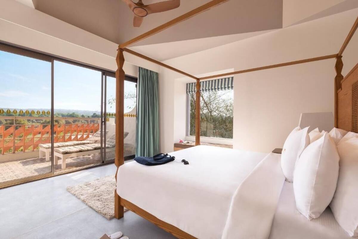 A four-poster bed with a view of a red fence and greenery outside.