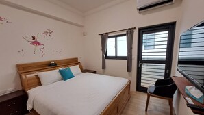 Um quarto com cama de madeira, uma pequena escrivaninha, uma cadeira, uma janela com cortinas e um ornamento na parede.
