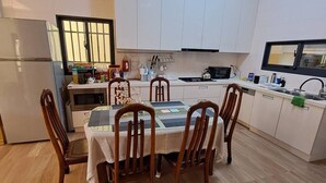 Uma cozinha moderna com armários brancos, uma mesa de jantar com cadeiras, uma geladeira e uma janela.