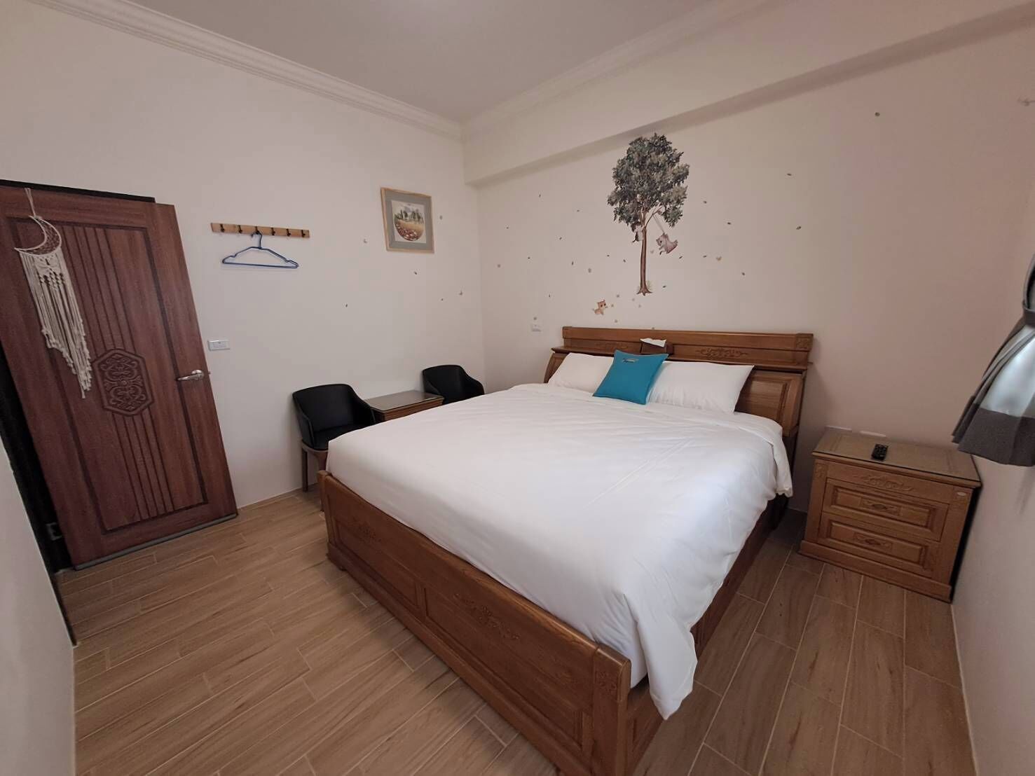 A bedroom with a wooden bed, two black chairs, a small table, a nightstand, and a door with a decorative handle.