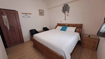 A bedroom with a wooden bed, two black chairs, a small table, a nightstand, and a door with a decorative handle.
