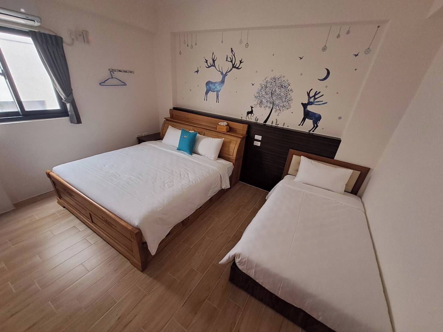 Une chambre avec deux lits, des têtes de lit en bois et une fresque murale représentant des animaux et des arbres.