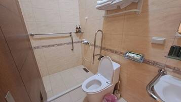 A bathroom with a toilet, sink, and shower. There are towels on a rack and toiletries on the wall.