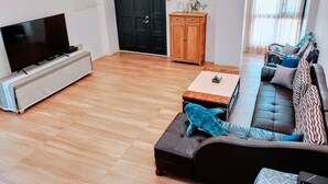 Uma sala de estar com uma televisão de tela plana, um sofá, uma mesa de centro e um armário de madeira.