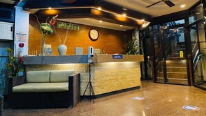A reception area with a counter, a clock, a ceiling fan, and a staircase. - Stonewood Hotel (General Santos)