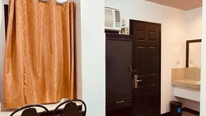 A room with a black wardrobe, a small desk with two chairs, a black trash bin, and a bathroom with a mirror and a shelf. - Stonewood Hotel (General Santos)