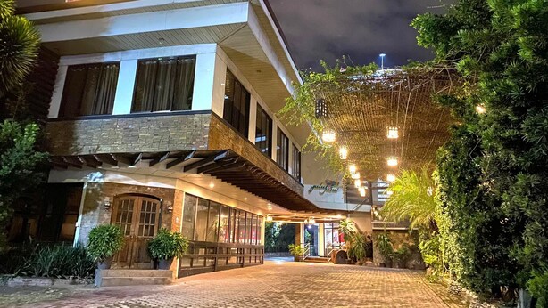 A two-story building with a stone facade, a covered outdoor area with a wooden deck, and a well-lit entrance. - Stonewood Hotel (General Santos)