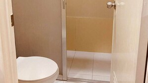 A bathroom with a toilet, a shower area, and a door. - Stonewood Hotel (General Santos)