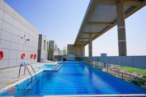 A rooftop swimming pool with a clear view of the sky, a modern architectural design, and a few lounge chairs. - Cozy apartment in Sport City (Dubai)