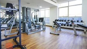 Een fitnessruimte met cardioapparatuur, gewichtbanken en dumbbells.