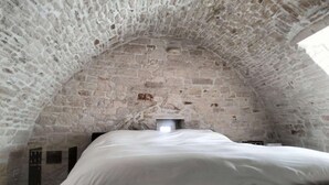 A bedroom with a stone vaulted ceiling, a bed, and a small window.