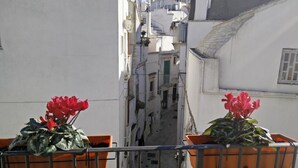 A narrow street between buildings with balconies, each with a potted plant.