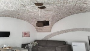 A living room with a stone ceiling, a grey sofa, a small table with a glass top, and a white air conditioner.