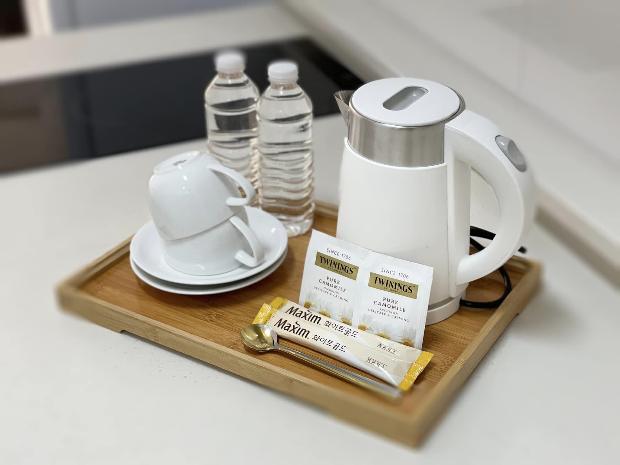 A tray with a white teapot, two water bottles, a white cup and saucer, and two Twinings tea packets on a wooden tray.