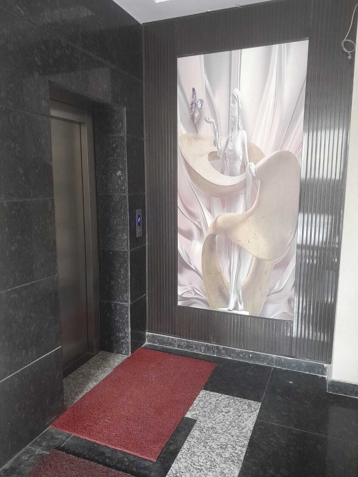 A modern elevator with a red carpet leading to it, a marble wall, and a large abstract artwork on the adjacent wall.
