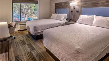 A hotel room with two beds, a desk, a chair, and a large window.
