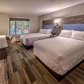 A hotel room with two beds, a desk, a chair, and a large window.